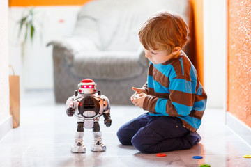 Little blond boy playing with robot toy at home, indoor.