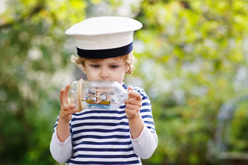 Happy kid boy in skipper uniform playing with toy ship