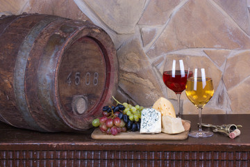 Glasses and bottles of wine, cheese on old  barrel