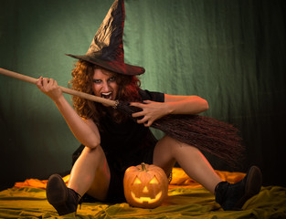 Woman dressed like a witch. She is with broom and pumpkin.