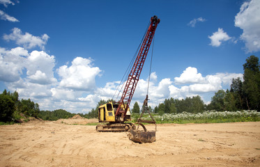 Fototapeta premium Excavator standing on sand near forest on summer day