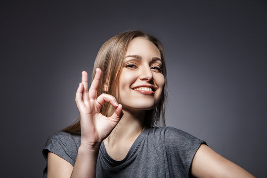 Smiling Woman With Okay Gesture On Dark Grey