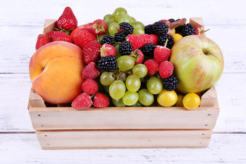Different berries and fruits in box on wooden table close-up