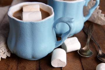 Cups of coffee with marshmallow and napkin on wooden table