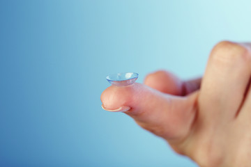 Contact lens on finger on blue background