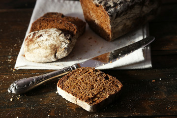 Sliced rye bread and knife on white napkin on wooden background