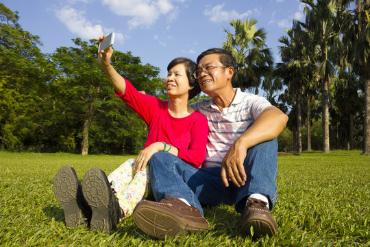 Asian Senior couple sitting on grassland and  taking picture