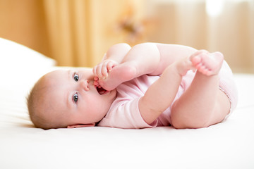 baby girl lying and  pulling her legs to her mouth - obrazy, fototapety, plakaty