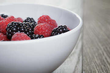 ripe blackberries and raspberries in white bowl on old oak table