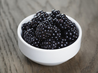 ripe blackberries in white bowl on old oak table