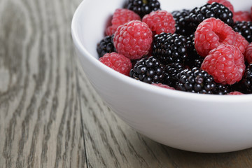 ripe blackberries and raspberries in white bowl on old oak table