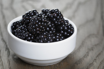 ripe blackberries in white bowl on old oak table