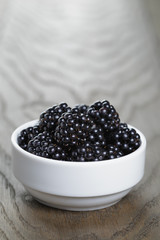 ripe blackberries in white bowl on old oak table