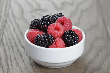 ripe blackberries and raspberries in white bowl on old oak table