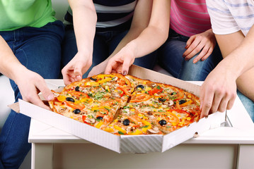 Group of young friends eating pizza in living-room on sofa