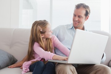 Casual father and daughter using laptop on the couch