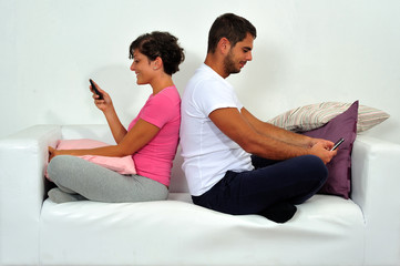 Couple back to back with smartphone on sofa