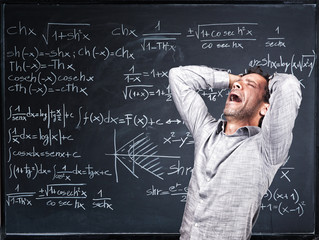  stressed and depressed teacher gets desperate in front of a slate blackboard with mathematical symbols. difficulty in learning and teaching.