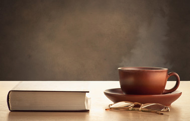 Obraz na płótnie Canvas Book, glasses and cup of hot tea on a dark brown background