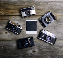 Vintage cameras around empty retro photograph on wooden backgrou