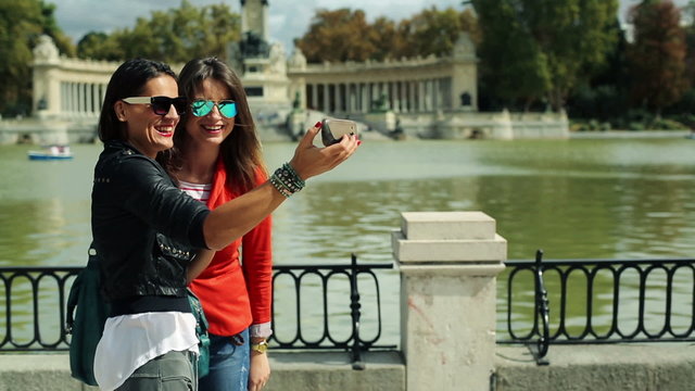 Happy girlfriends taking photo with cellphone in park in Madrid