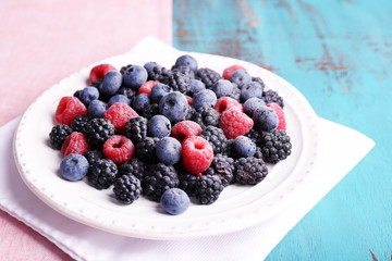 Iced berries on plate, on color wooden background