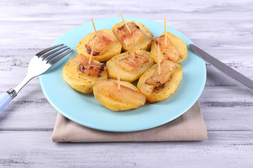 Baked potato with bacon on plate, on wooden background