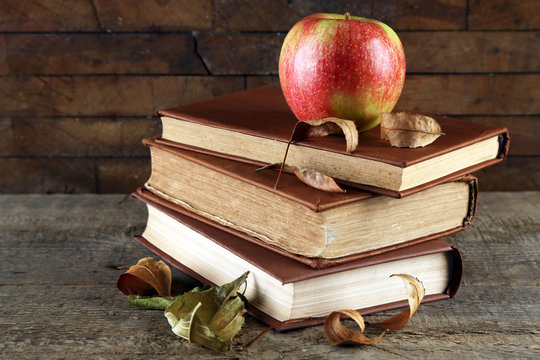 Apple with books and dry leaves on wooden background