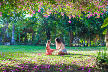 Young mother with little daughter in the lush garden and enjoy