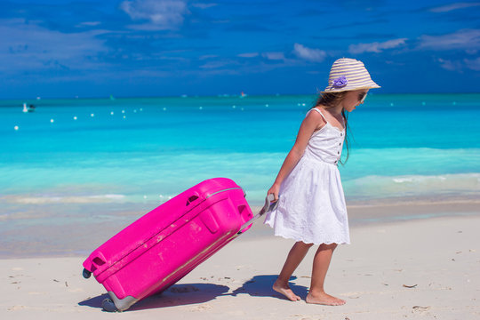 Little adorable girl with big luggage in hands on tropical beach