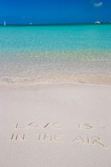 Love is in the air written on tropical beach white sand