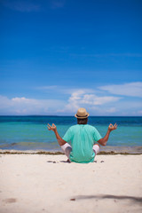 Young man sitting in lotus position on white tropical beach