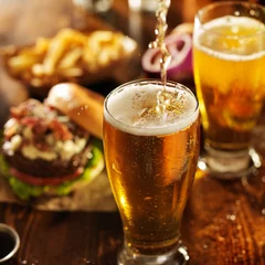 Door stickers Beer pouting beer into glass with burgers on wooden table top