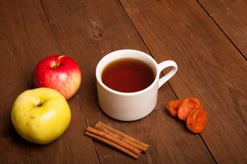 Cup of tea on old wooden table with two apples, dried apricots a