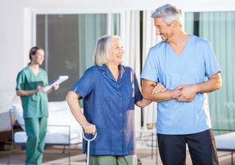 Happy Nurse Assisting Senior Woman To Walk