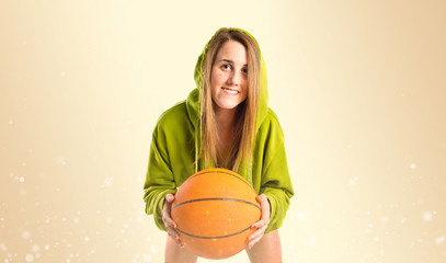 Blonde girl playing basketball over ocher background