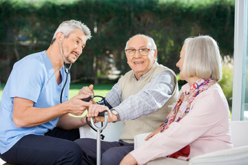 Woman Looking At Male Doctor Measuring Blood Pressure