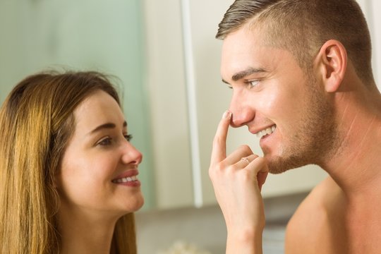 Cute woman putting cream on boyfriends nose