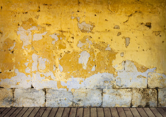 Rough wall with peeling yellow paint and wooden floor