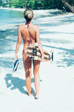 Young woman with longboard in hand walking on white sand