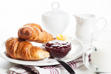 Croissants with butter and a glass of milk on a plate