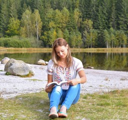 Beautiful young woman reading a book near a lake
