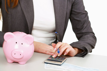Young woman with a piggy bank and using a calculator.