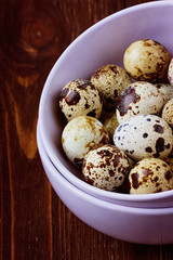 Quail eggs in a ceramic bowl on a brown wooden surface