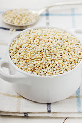 Pearl barley in a white ceramic bowl on a wooden background