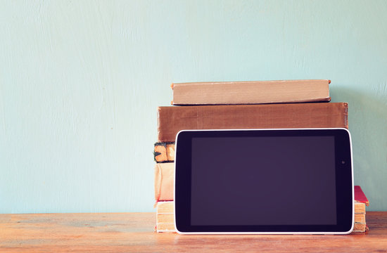 Stack Of Old Books And Tablet Over Wooden Shelf. New Technology 