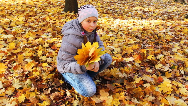 nice teen girl sits squatted and holds yellow leaves in park
