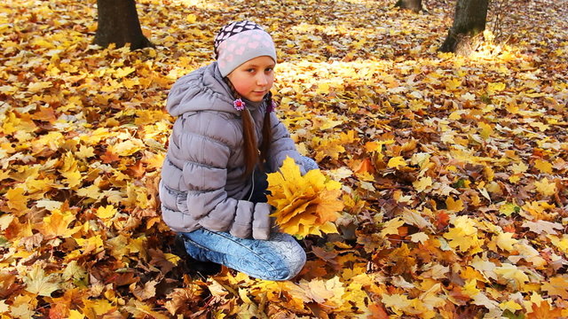 nice teen girl sits squatted and collects yellow leaves in park