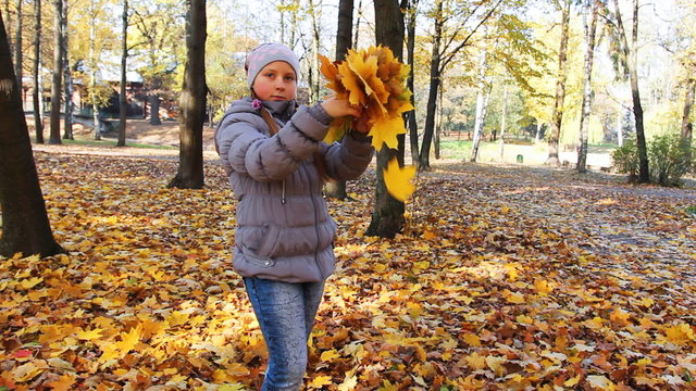nice teen girl stands and scatters yellow leaves in city park