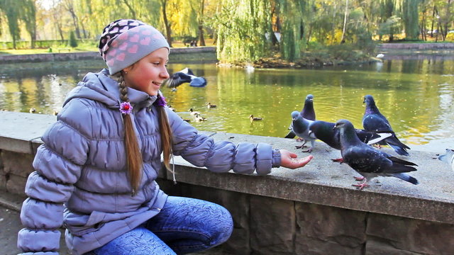 cute teen girl siting feeds pop-corn pigeons from hand, closeup